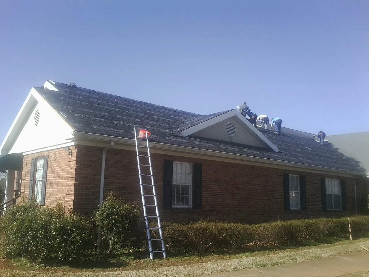 Crew tearing shingles off a brick ranch roof with a ladder set — Emergency Roof Repair work by our crew in Payette