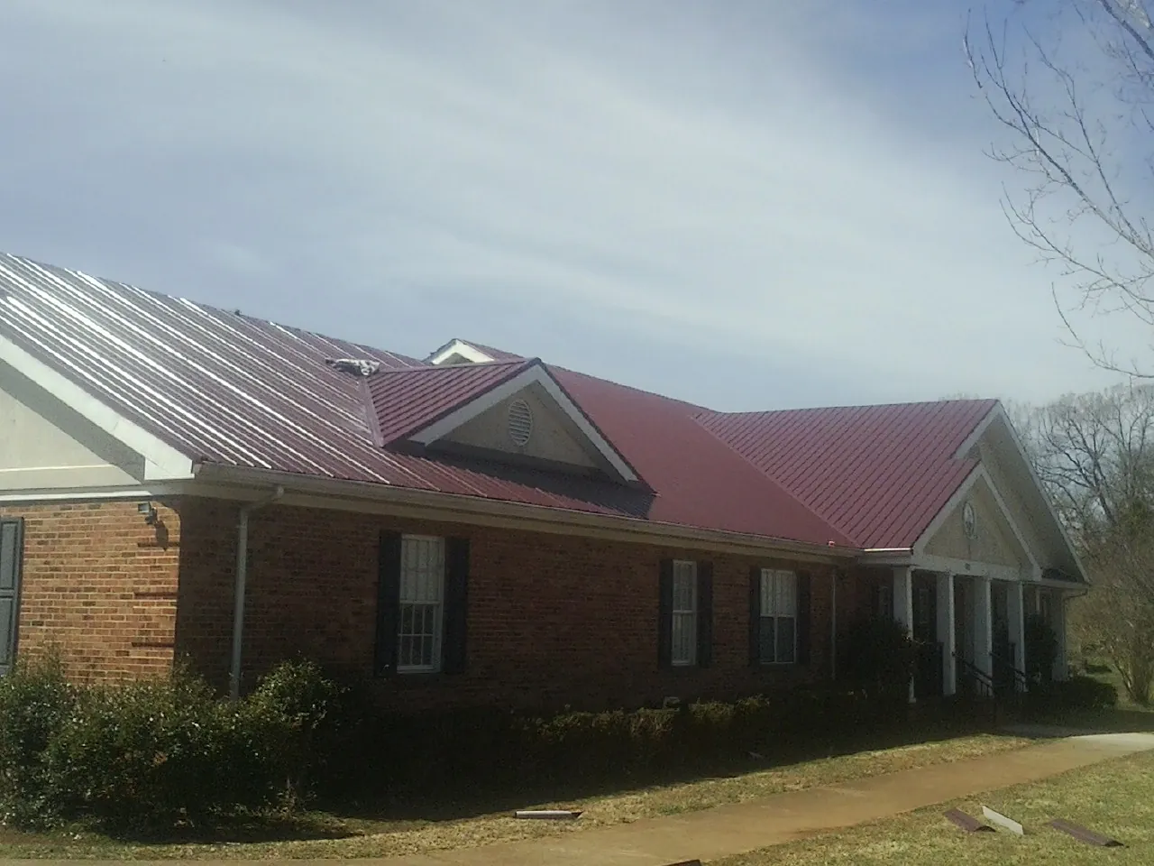 Red metal roof with gabled entries on a long brick building, from a Hail Damage Roof Repair job in Payette