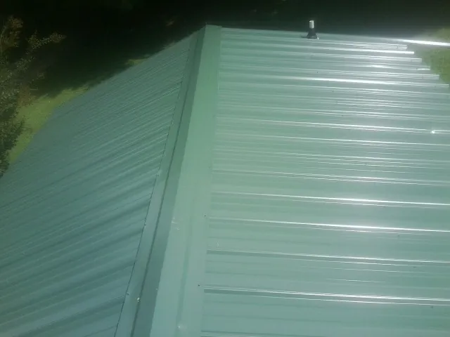 New green metal panels meeting at the ridge of a roof — Flat Roof Repair work by our crew in Payette