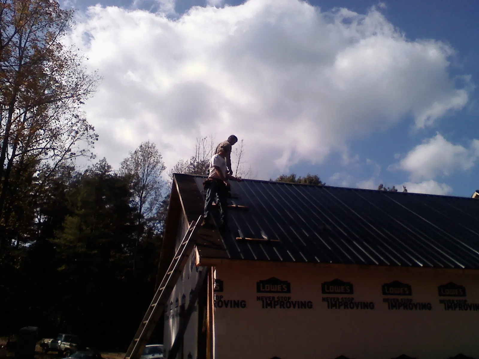 Roofer fastening dark metal panels high against a cloudy sky, from a Roof Inspection job in Payette