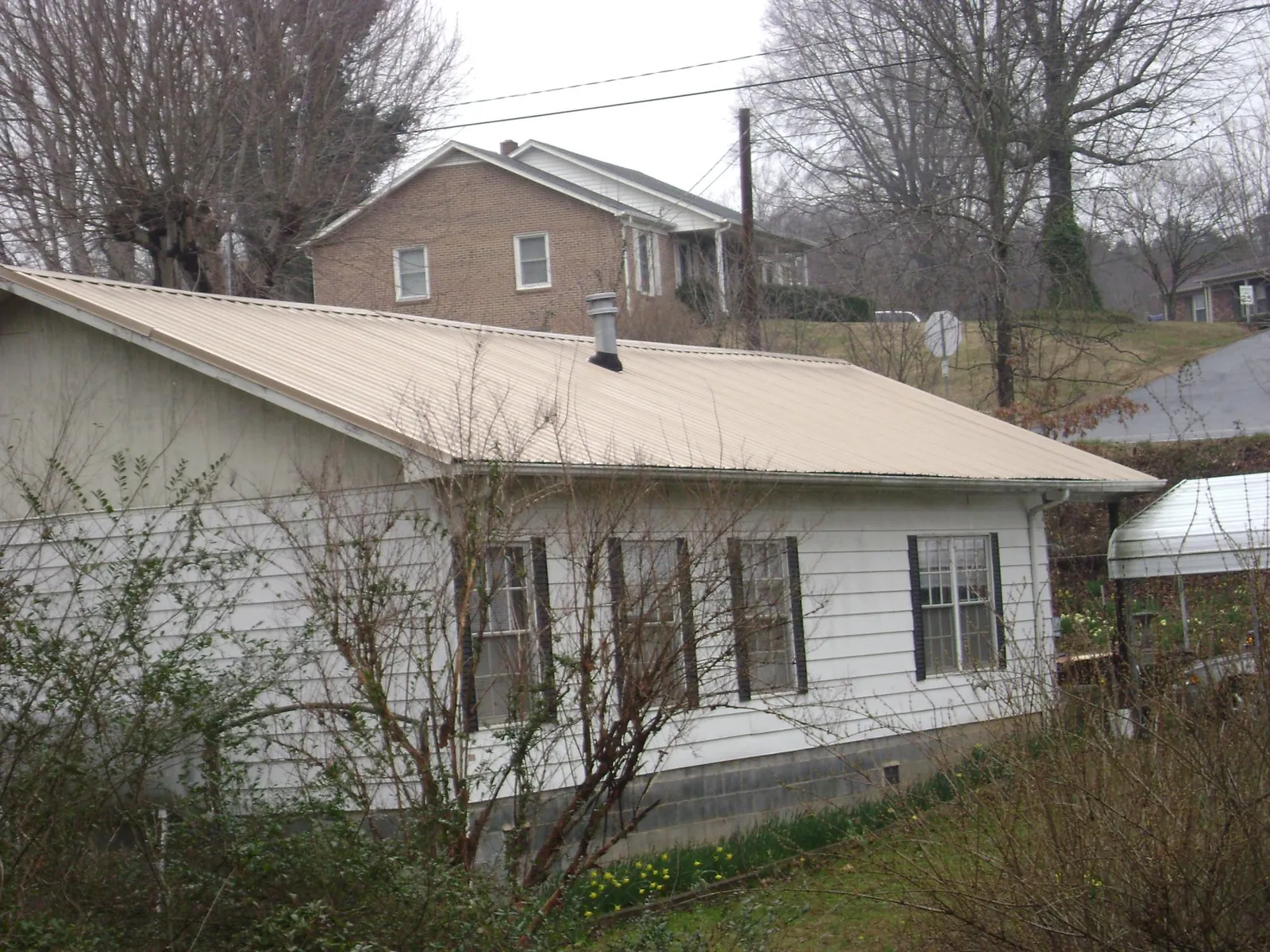 Tan metal roof on a white sided house set into a hillside — Commercial Roofing by Roofing Brothers in Payette